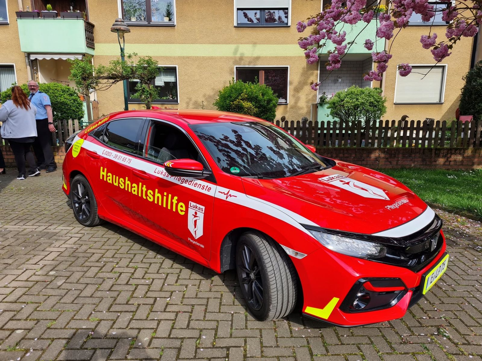 Rotes Lukas-Fahrzeug mit zwei Mitarbeitern